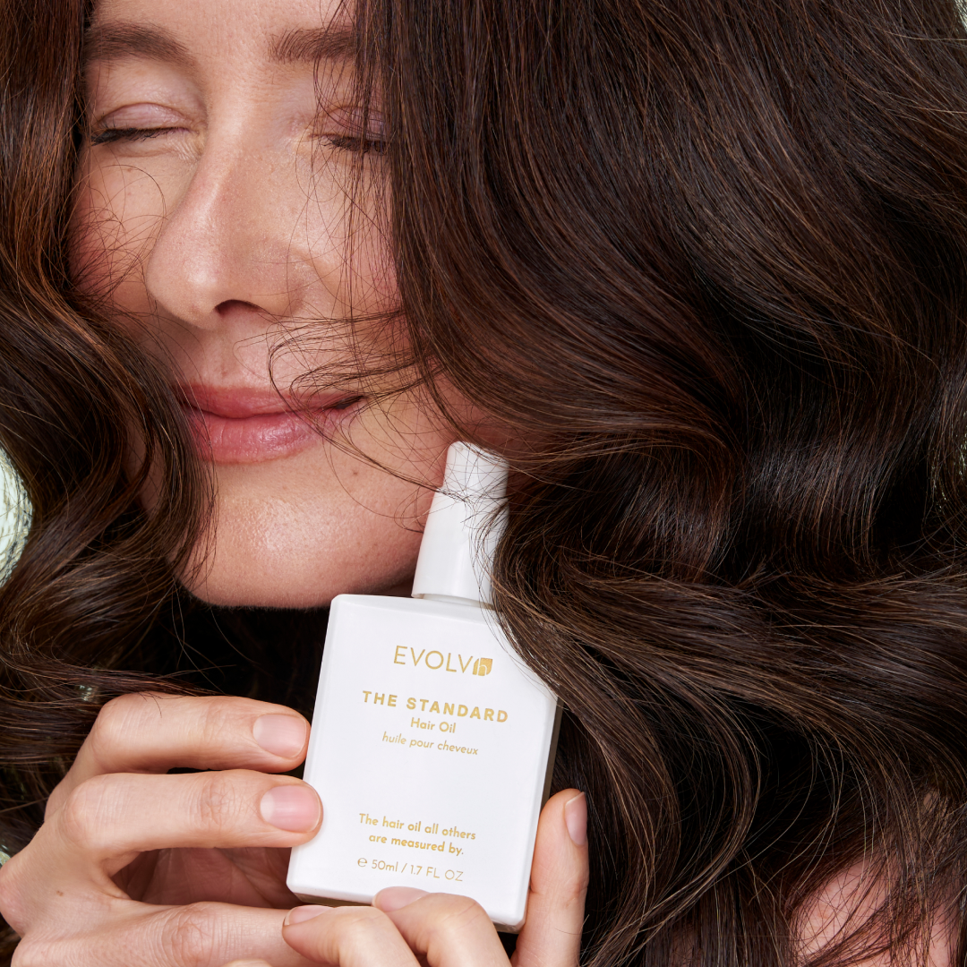 Woman with wavy hair holding EVOLVh The Standard Hair Oil